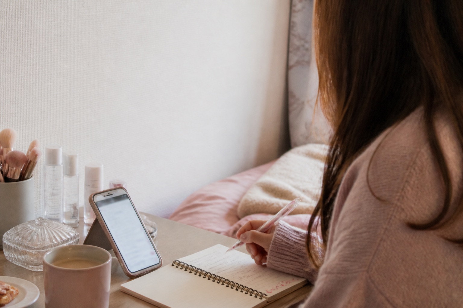 ピンクの部屋でスマートフォンと日記ノートを開くイメージ